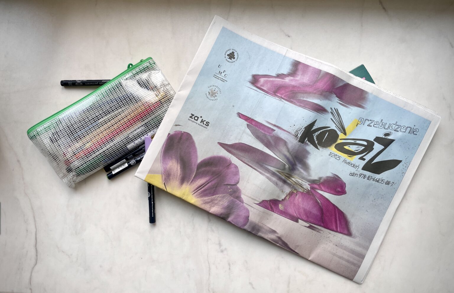 Zdjęcie przedstawiające gazetę Kolaż na płaszczyźnie, obok widoczne długopisy, mazaki